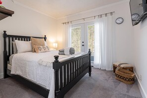 A bedroom with a black-framed bed, a bedside lamp, a window with curtains, a clock on the wall, and a wicker basket.