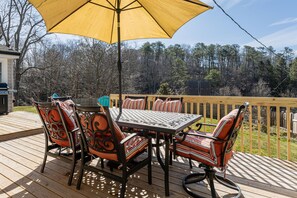 An outdoor deck with a table and chairs, a yellow umbrella, and a view of trees.
