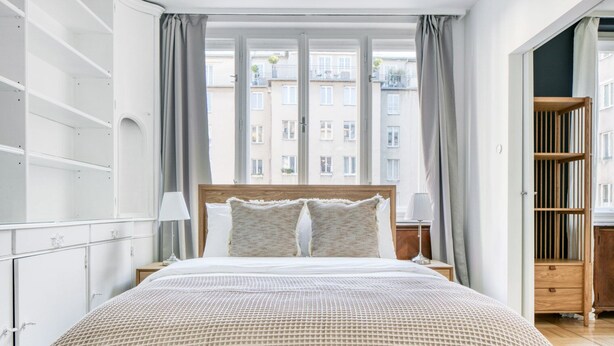 A modern hotel room with a large bed, a wooden headboard, and a view of buildings through the window. - Dreamy Innere Stadt 2BR w/ Elevator, steps to Hoher Markt, by Blueground (Vienna)