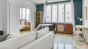 A modern living room with a sofa, a dining table, and a workspace with a chair. There is a window with curtains, a radiator, and a bookshelf. - Dreamy Innere Stadt 2BR w/ Elevator, steps to Hoher Markt, by Blueground (Vienna)