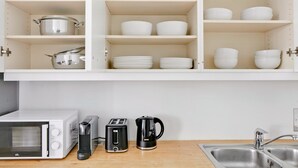 Una cocina con gabinetes blancos, microondas, tostadora, cafetera y un lavamanos.