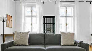 Una sala de estar moderna con un sofá gris, dos almohadas blancas, una mesita con un libro y una estructura metálica negra en el centro.