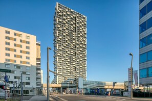Een modern hoog gebouw met een unieke gevel, omgeven door stedelijke infrastructuur.