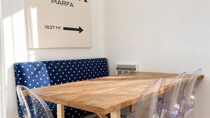A dining area with a wooden table, clear plastic chairs, a polka-dotted bench, and a wall-mounted sign with the text 'PRADA MARFA 1837 MI'.
