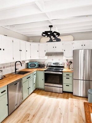 A modern kitchen with white cabinets, stainless steel appliances, and a wooden countertop.