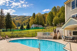 A swimming pool with a wooden deck, lounge chairs, and a view of a mountainous landscape.