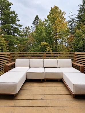 A sectional sofa with a wooden deck and a backdrop of trees.