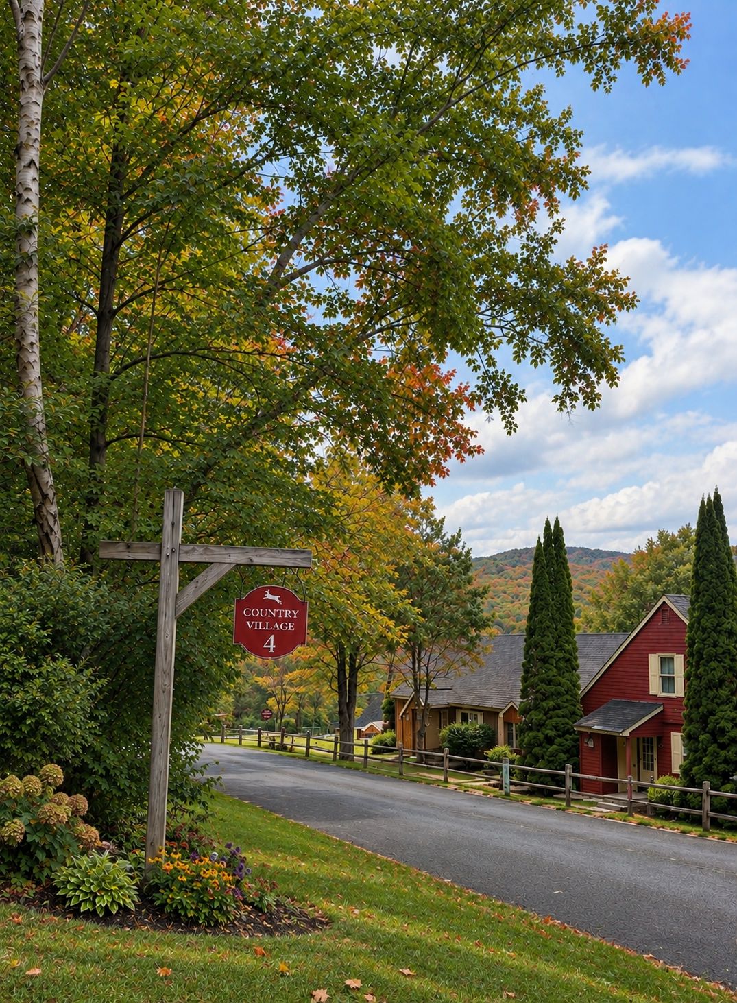Un panneau indiquant l’entrée d’un village, une route et des maisons, avec en arrière-plan des arbres et des collines.