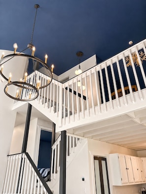 Un interior de varios niveles con escalera, barandas blancas y un candelabro.