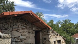 A stone building with a red roof, a wooden door, and a stack of firewood in front.