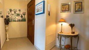 Un corridoio con una porta in legno, un quadro incorniciato, un tavolo con una lampada e un vaso con fiori.