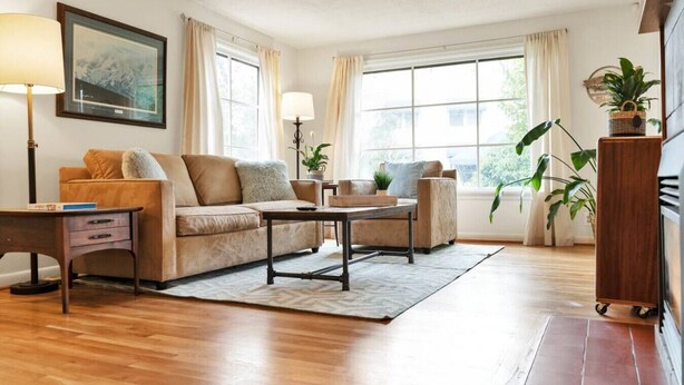 A living room with a sofa, two armchairs, a coffee table, a side table, and a lamp. There are windows with curtains, a plant, and a framed picture on the wall. - Mellow Yellow UW & Children's  Free parking! (Seattle)