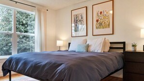 A bedroom with a large bed, a nightstand, a dresser, and two framed floral paintings on the wall. - Mellow Yellow UW & Children's  Free parking! (Seattle)