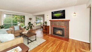 A spacious living room with a fireplace, large windows, and a television mounted on the wall. - Mellow Yellow UW & Children's  Free parking! (Seattle)