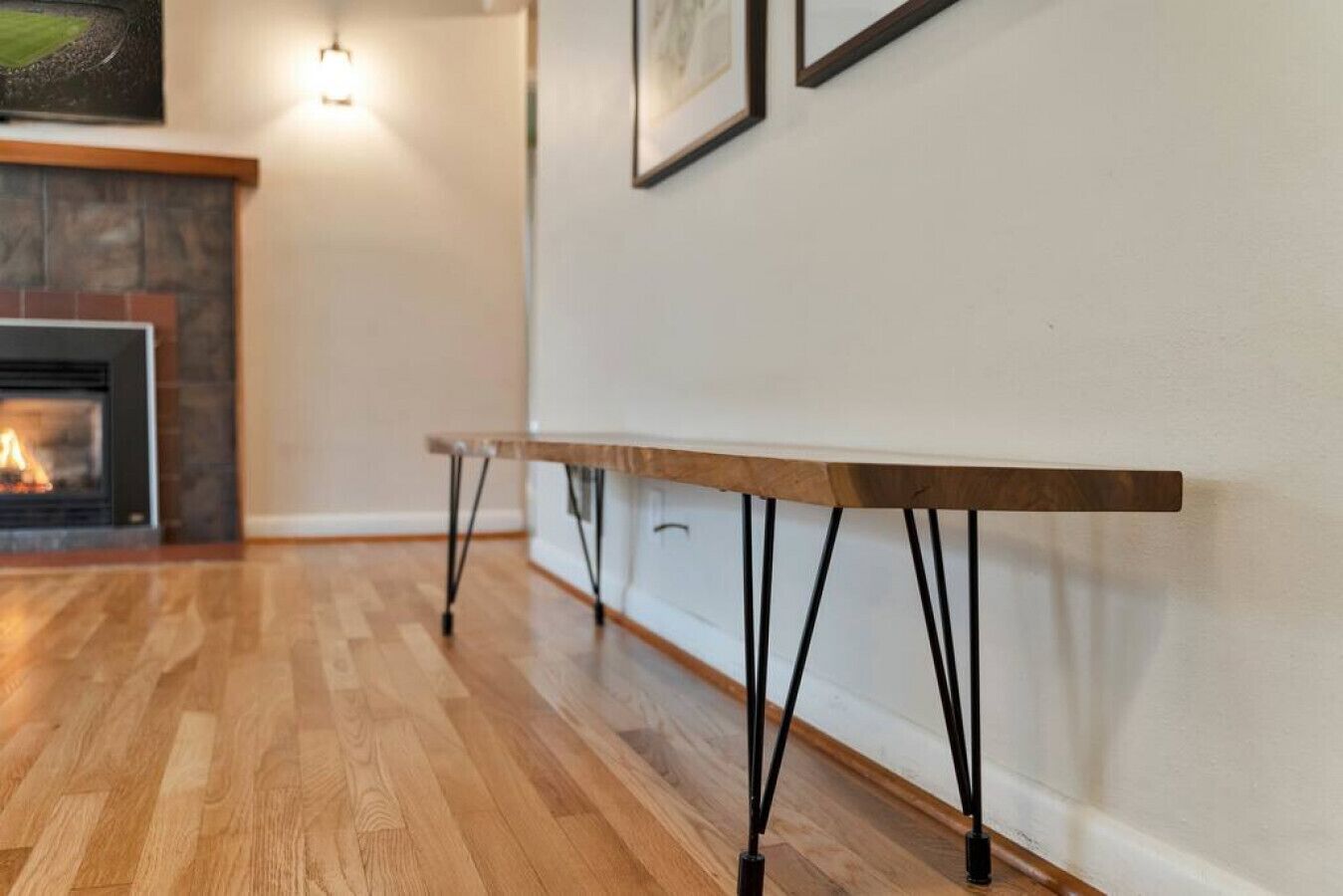 A room with a wooden floor, a fireplace, and a long table with black legs.