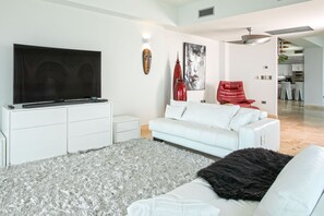 A modern living room with a flat-screen TV, a white sofa, a red chair, and a grey shag rug.