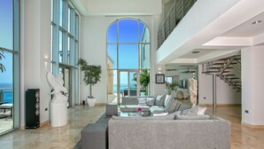 A spacious living room with a large sectional sofa, a coffee table, and a view of the ocean through a large arched window. - The Cove | Beach Front - Located in  Exquisite Simpson Bay with House Cleaning Included (Lowlands)