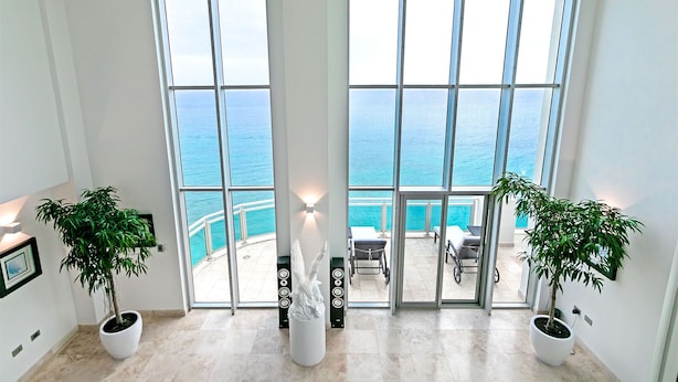 A room with large windows overlooking a pool and the sea. There are two potted plants and a white sculpture. - The Cove | Beach Front - Located in  Exquisite Simpson Bay with House Cleaning Included (Lowlands)