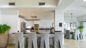 A modern kitchen with stainless steel appliances, a central island, and a dining area with grey upholstered chairs. - The Cove | Beach Front - Located in  Exquisite Simpson Bay with House Cleaning Included (Lowlands)