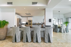A modern kitchen with stainless steel appliances, a central island, and a dining area with grey upholstered chairs.