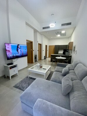 A modern living room with a grey sofa, a coffee table, and a TV displaying 'EMILY IN PARIS'.