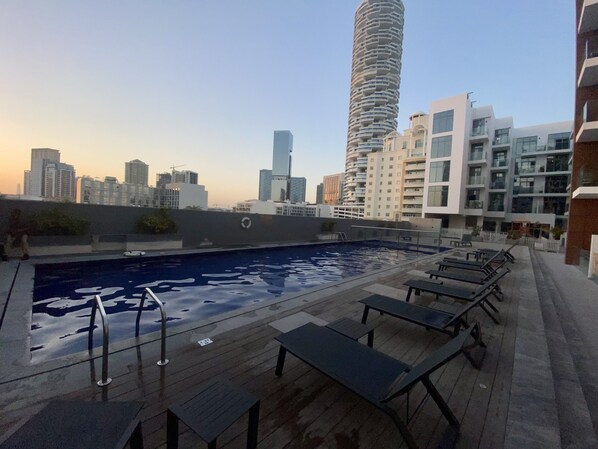 A rooftop pool area with lounge chairs and a city skyline in the background.