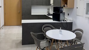 Een moderne keuken met grijze kastjes, een zwarte magnetron en een wit aanrecht. Er staat een ronde tafel met vier stoelen en een kleine witte vaas.