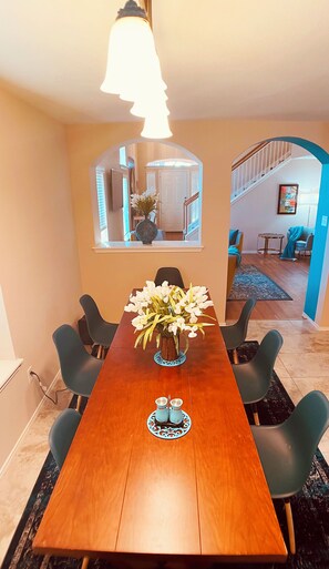 Un comedor con una larga mesa de madera, seis sillas, un jarrón de flores y una araña.