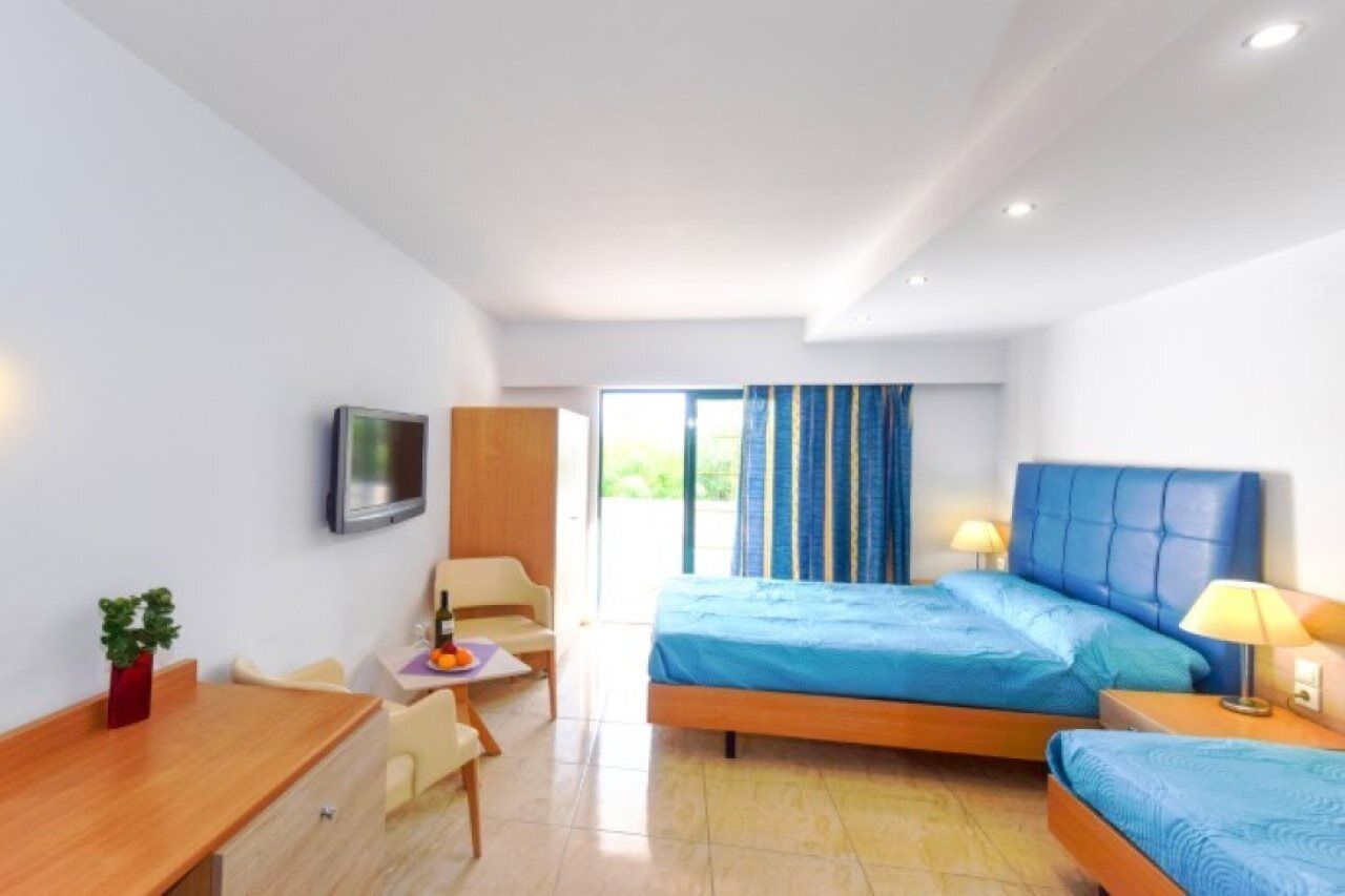A hotel room with a bed, a desk, a chair, a TV, and a window with curtains.