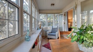 A sunlit room with large windows, a wooden table, a chair, a bookshelf, and a potted plant. - Riverside Cottage: Close to Ocean and Myrtle Beach (Murrells Inlet)