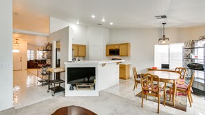 Una cucina moderna con mobili bianchi, un'isola centrale e un'area pranzo con sedie e tavolo in legno.