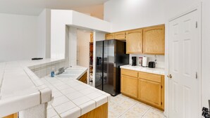 Una cucina moderna con piastrelle bianche, un frigorifero nero, mobili in legno e un piano di lavoro bianco.