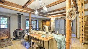 A cozy room with a wooden ceiling, a central table, a fireplace, and a large window. - Pet-Friendly Cabin: Minutes to Gig Harbor! (Fox Island)