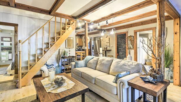 A cozy living room with a wooden staircase, a sofa, a coffee table, and a dining area. - Pet-Friendly Cabin: Minutes to Gig Harbor! (Fox Island)