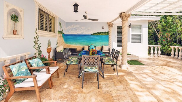 A patio with a dining table, chairs, and a view of the ocean.