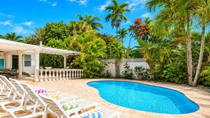 A swimming pool with lounge chairs, surrounded by palm trees and a white fence.