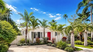 A residential property with a paved driveway, palm trees, and a red door.