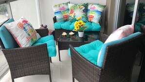 Un balcon agrémenté de meubles en osier, de coussins turquoise et d’une table ornée d’un arrangement de tournesols.