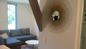 Een moderne woonkamer met een grijze modulaire bank, een ronde spiegel en een houten vloer.
