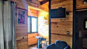 Interno di una baita in legno con una televisione montata a parete, una finestra e una poltrona.