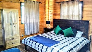 Camera da letto in una baita di legno, con un letto, tende, un armadio e un comodino.