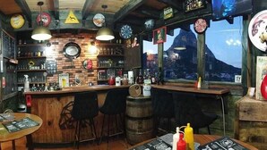 Un bar con arredi in legno, scaffali pieni di bottiglie e vista su una montagna.