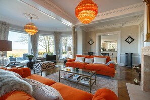 A spacious living room with a large orange sofa, a glass coffee table, and a chandelier.