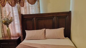 A neatly made bed with a wooden headboard, a bedside table with a vase of flowers, and a curtain with a floral pattern. - 2-Bed, Sleeps 4, Private Garden, Parking (Portmore)