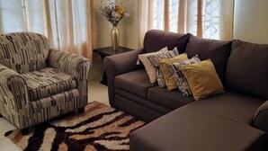 A living room with a striped armchair, a brown sofa with patterned cushions, and a decorative vase on a side table. - 2-Bed, Sleeps 4, Private Garden, Parking (Portmore)