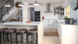 A modern kitchen with a central island, bar stools, stainless steel appliances, and a clock on the wall. - Manilva Coastal Retreat for over 50 's (Manilva)