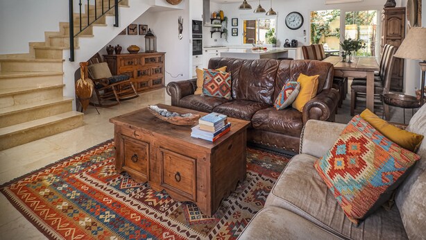 A spacious living room with a brown leather sofa, a wooden coffee table, and a patterned rug. A staircase with a wooden railing leads to an upper level. - Manilva Coastal Retreat for over 50 's (Manilva)
