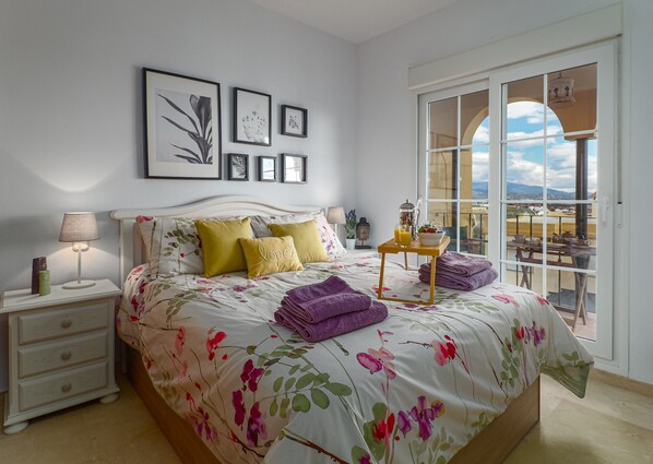 A bedroom with a bed, bedside table, and a view of the outside balcony.