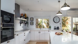 A modern kitchen with white cabinets, a built-in oven, a large island, and a window with a view of greenery. - Manilva Coastal Retreat for over 50 's (Manilva)