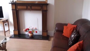 A living room with a brown leather sofa, a small table, and a fireplace with a vase of flowers. - Grand 4-Bed Quasi semi House in Manchester (Manchester)